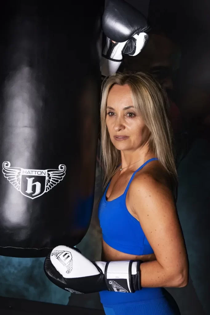 Female personal trainer in Bromley wearing boxing gloves next to punching bag in private gym